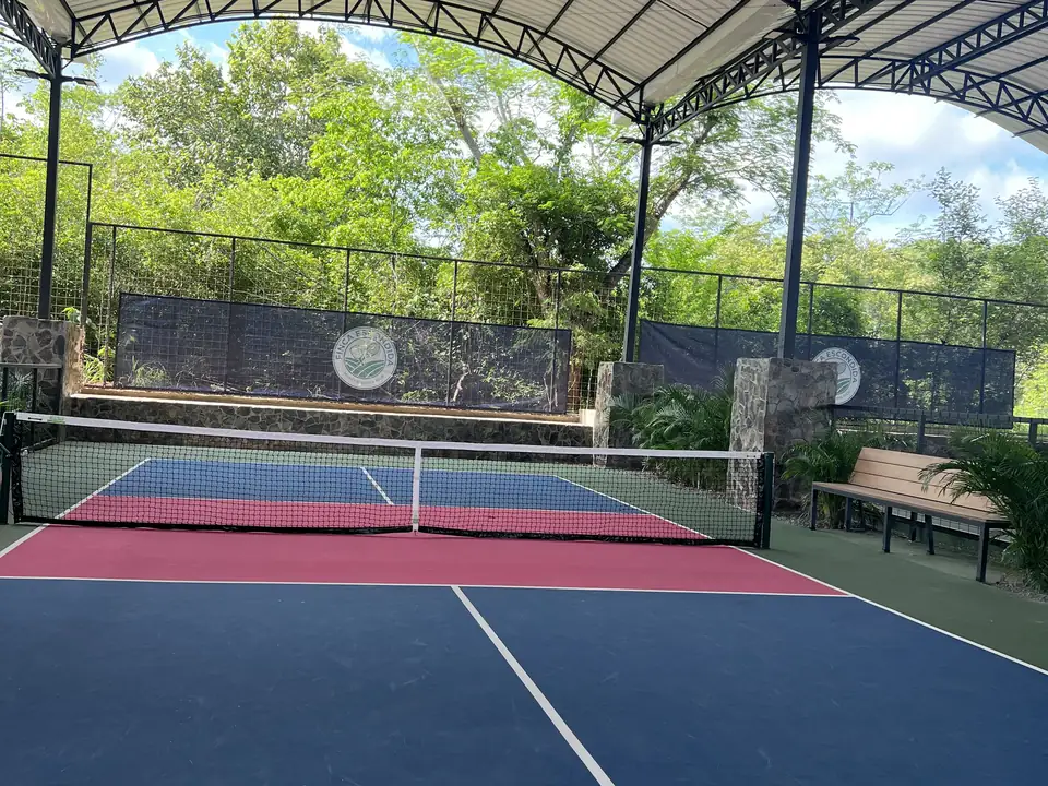 Covered pickleball court under the arched roof at Finca Escondida, the club crest on the back wall
