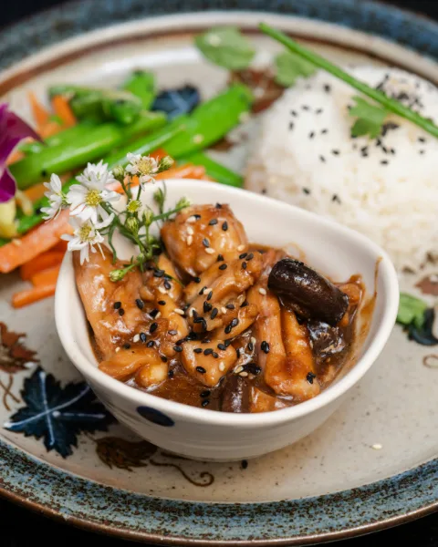 Braised chicken with mushrooms and sesame in a small bowl, with rice and stir-fried greens