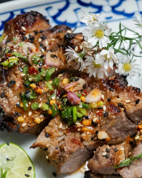 Grilled pork with chili, shallot and herbs, lime wedges on the side
