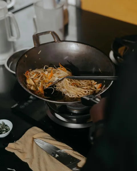 Rice noodles being tossed in a wok over the flame