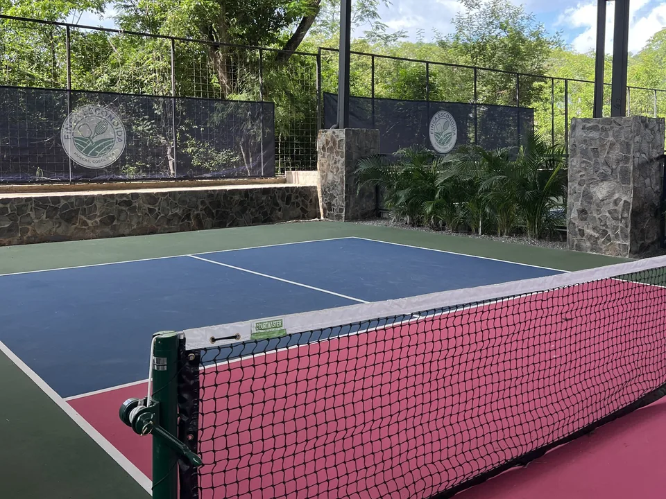 Pickleball net on a covered court, the club crest on the stone wall behind