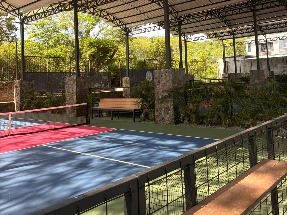 Covered pickleball court in dappled shade, with a courtside bench
