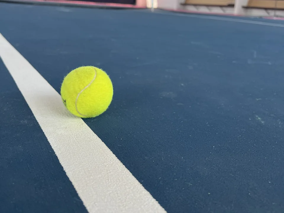 Tennis ball on the line of a blue court under the roof