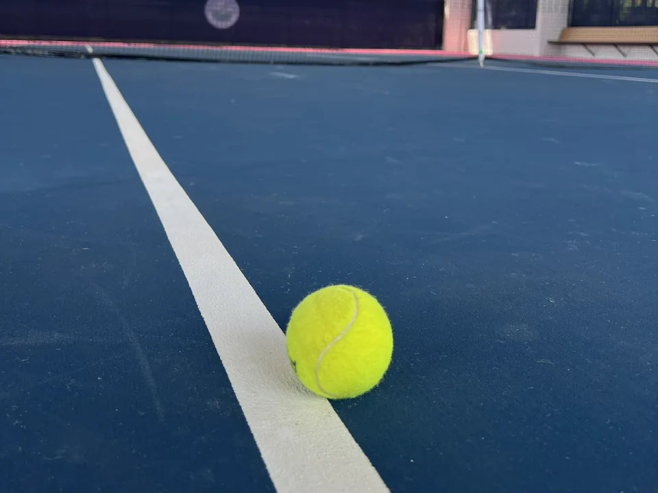 Tennis ball resting on a line of a covered court, the net behind